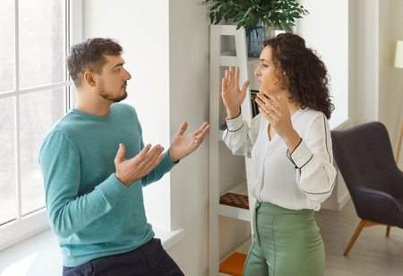 Frustrated angry young couple arguing with each other. Annoyed woman raising hands while emotional...