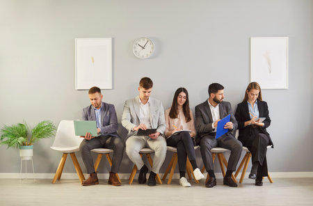 Young hr applicants sitting in queue preparing for important interview in office, vacancy candidates waiting on chairs holding resume, human resources, people hiring and job search, worried beforeの写真素材