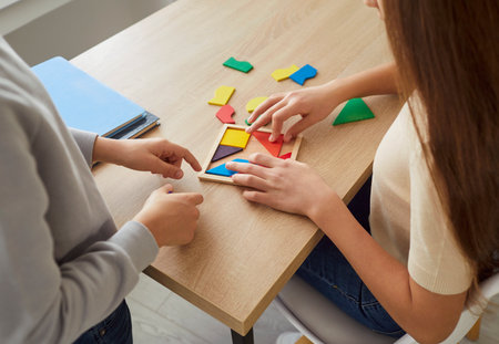 Closeup top view of children hands collecting wooden colorful geometric figures sitting at table at home. Kids solving an educational puzzle indoors. Education and leisure concept.の写真素材