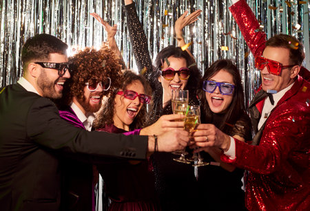 Young friends group having fun at disco clanging glasses together at party drinking champagne. Happy cheerful people in suits celebrating success at corporate party on silver foil background.の写真素材