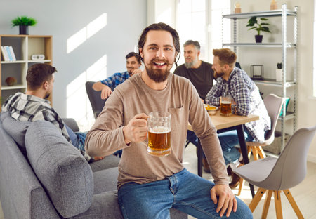 Group of happy friends drinking beer at home together. Cheerful men partying, drinking beer drinks, talking to each other. Portrait of hipster young man mustache looking at camera with partners behindの写真素材