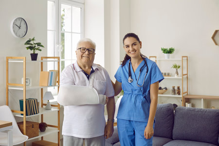 Portrait of happy injured senior male patient together with female doctor. Old man with arm sling...