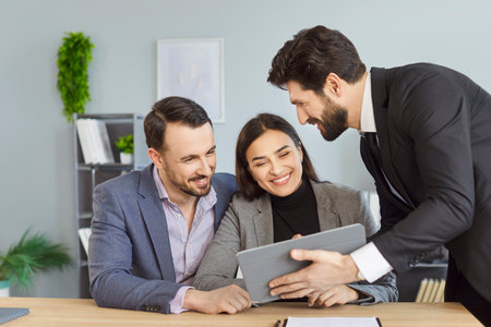 Young couple sitting at the desk discussing contract and having consultation with man realtor or...