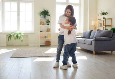 Happy children of different age standing in living room and hugging each other with warmth and tenderness. Smiling sibling embracing, showing care, closeness, emotional connection and family bond.の写真素材