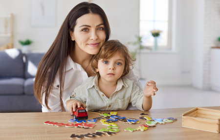 Mother, young babysitter and little child playing logic strategy wooden board game at table together, caring mom teaching kid boy, happy family engaged in educational activity at home, learningの写真素材