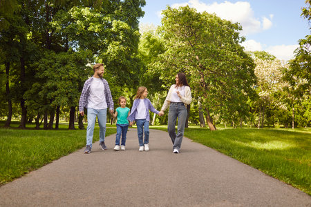 Smiling young happy family of four with two children boy and girl walking outdoors and talking with each other. Cheerful parents and kids enjoying nature during a walk in summer park.の写真素材