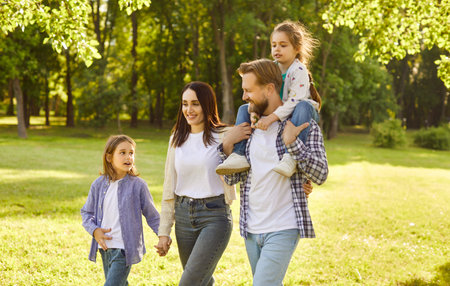 Happy smiling family of four with two kids boy and girl walking in summer park enjoying beautiful...