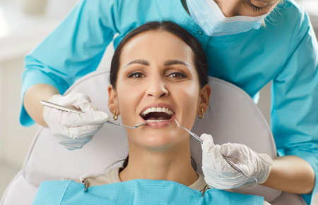 Doctor dentist examines woman patient oral care during clinic visit, focusing on dental treatment and dentistry in a professional setting with attention to health and wellness support.の写真素材