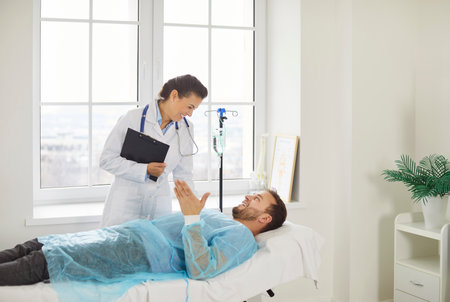 Female doctor talks with man patient, happy to announce good results after curing disease, consulting and giving recommendations, posing in clinic. Medical advice and health care conceptの写真素材