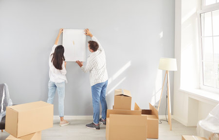 Family couple hanging a picture together on the wall while decorating new home or apartment during relocation or moving. Highlighting teamwork, creativity, and joy in moving process.の写真素材