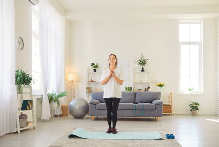 Full length portrait of a senior elderly woman wearing sportswear standing on yoga mat in living room at home going to do sport exercises. Exercising in retirement, fitness, workout concept.の写真素材