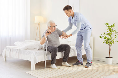 Doctor or caregiver supports a senior patient in a nursing home, helping them walk during rehabilitation. Healthcare moment highlights essential care, assistance, and recovery support.の写真素材