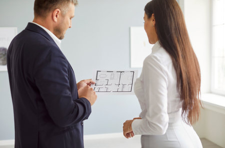 Real estate agent or realtor discusses the blueprint of a new home or office with a client. The project review highlights the planning stage for a property purchase, showcasing teamwork.の写真素材