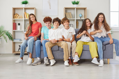 Group of happy and diverse students or friends sits together on a couch, enjoying leisure time and fun. The kids are bonding, showcasing strong friendship and joy in this lively setting.の写真素材