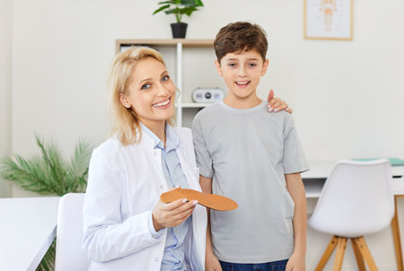 Female orthopedist in clinic hugs boy, close-up. Selection of comfortable orthopedic insole. Concept child pediatrician, doctor diagnose, pediatric orthopedic, medical comfortの写真素材