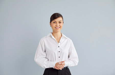 Portrait of happy smiling young business woman isolated on gray studio background and looking cheerful at camera. Smart joyful girl wearing formal clothes standing indoors with copy space.の写真素材