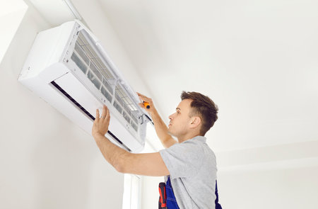 Air conditioning indoor unit installed by qualified installation technician. Professional young electrician maintaining, cleaning modern air conditioner on wall, room repairing, installing conditionerの写真素材