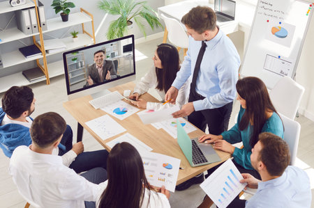 Professional business marketing team having a work meeting in the office, sitting around a table, and having a video call with their manager. Remote communication, teamwork conceptの写真素材