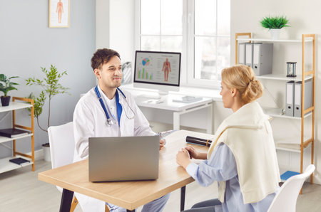 Positive male doctor or nurse is in consultation with a female patient in a hospital office, providing medical advice and quality care. Effective communication and healthcare delivery.の写真素材