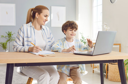 Mother helping son with homework, assisting with online education using a laptop. Supportive role of a mother in son learning journey, fostering a happy and educational family environment.の写真素材