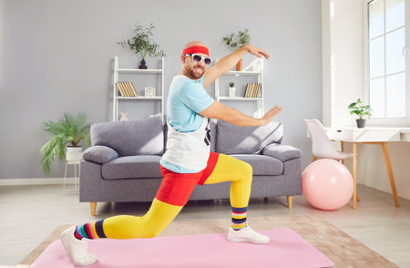 Funny man in a retro sportswear enjoys a fitness session at home, dancing and exercising. His workout routine combines sport and training, bringing joy and energy to his home gym activities.の写真素材