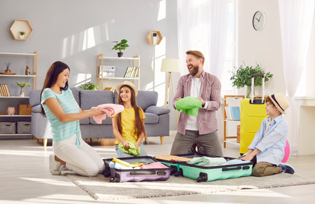 Happy young family of four with two kids boy and girl packing suitcases preparing for summer vacation trip sitting on floor at home together. Travelling, holiday and journey concept.の写真素材