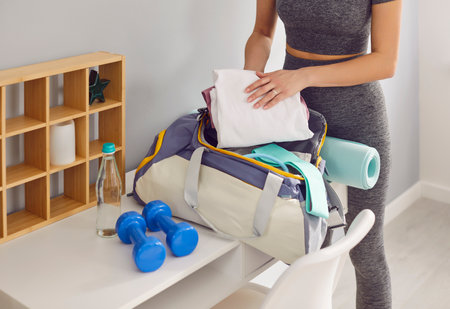 Sporty slim woman packing gym bag for sport exercising. Young athlete girl in sportswear preparing stuff for training packing sports supplies for active day. Wellness and healthy lifestyle concept.の写真素材