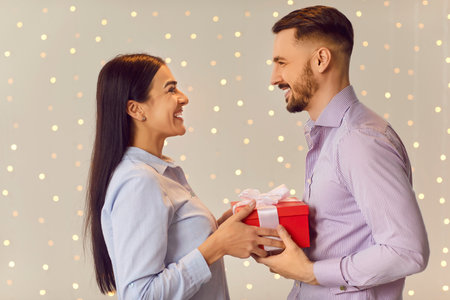 Happy husband giving a gift box to his amazed young wife on Valentine Day, anniversary or birthday. The love, romance, and relationship are beautifully captured with tenderness and joy.の写真素材