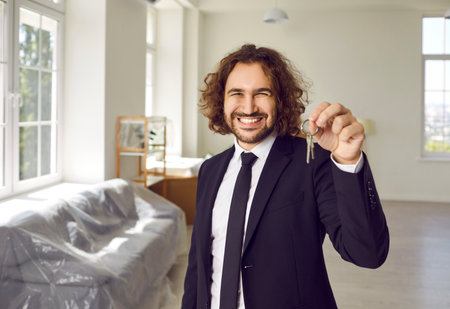 Portrait of a young smiling attractive bearded man with keys in his hands looking at the camera in new house . Real estate agent or happy joyful new homeowner enjoying real estate purchase.の写真素材
