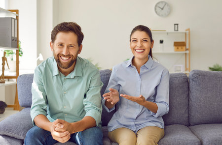 Portrait of happy couple looking and smiling at camera making video call together sitting on couch at home chatting with friends online at webcam. Concept of video call, internet connection.の写真素材