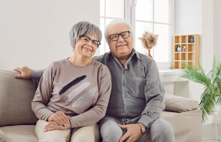 Portrait of a happy senior family couple wife and husband sitting on sofa in the living room at home. Two smiling gray-haired retired man and woman enjoying time together on retirement.の写真素材