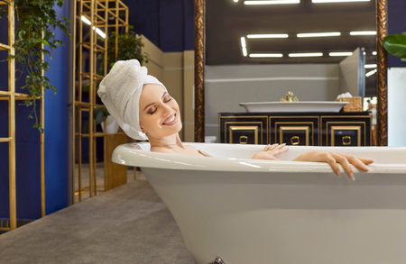 Portrait of relaxed beautiful young woman enjoying while taking bath in modern luxury bathroom. Female person in towel on head relaxing in bathtub. Body care, hygiene and wellness conceptの写真素材