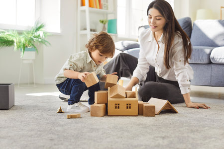 Young happy mother playing with educational wooden toys with cute little child boy in the living room at home. Female parent spending time with son. Family leisure and people concept.の写真素材