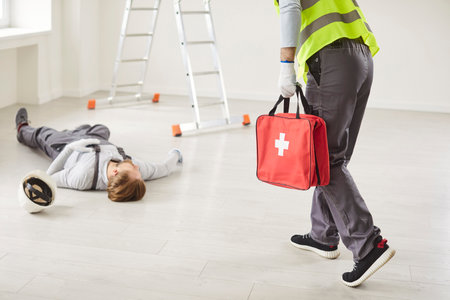 Young man worker hurrying to injured unconscious man constructor lying on the floor on building site after job accident and going to give him first aid. Emergency and safety concept.の写真素材