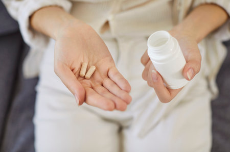 Woman taking daily medication or food supplements. Closeup hands of young girl on sofa at home holding plastic jar container and multivitamin pills or influenza and cold meds. Medicine, drugs conceptの写真素材