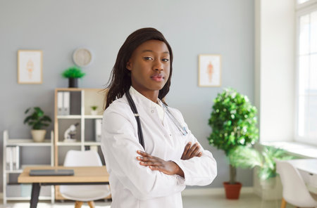 Beautiful confident African American woman doctor, female nurse posing for camera standing in modern clinic examination room, practitioner portrait of professional medical worker in hospitalの写真素材