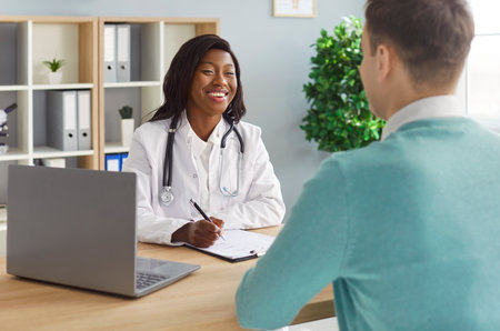 Positive african american doctor or nurse in hospital conducting consultation and appointment with patient. Healthcare aid and communication during medical visit. Professional support.の写真素材