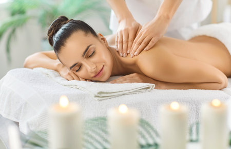 Satisfied woman enjoying back massage during spa treatment in salon, relaxing scene with luxury therapy, enhancing body care and comfort in a serene space filled with wellness and relaxation.の写真素材