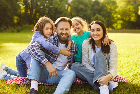 Happy family sitting together on plaid in nature, enjoying picnic time in park, smiling gladfully, having nice time together during summer, taking memorable photo. People, rest, vacationの写真素材