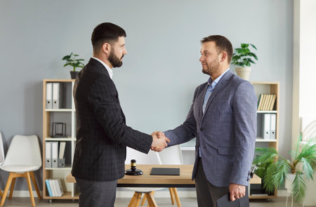 Male lawyer working on workplace shaking hands with client after consultation. Confident advocate reaching agreement with man standing in office. Legal law, jurisdiction and advice concept.の写真素材