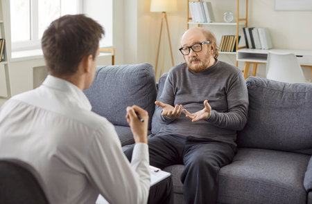 Elderly man patient joins therapy session with psychologist, engaging in conversation for depression recovery, receiving assistance through supportive dialogue in a space for emotional healing.の写真素材