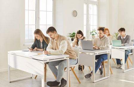 Group of young confident students sitting at the desk and writing test during a college or university lesson in classroom. People studying on project. Education and knowledge concept.の写真素材