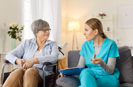 Elderly patient in a wheelchair receiving a medical consultation from a doctor or nurse at a hospital or nursing home. Healthcare, support, and professional care for disabled people.の写真素材