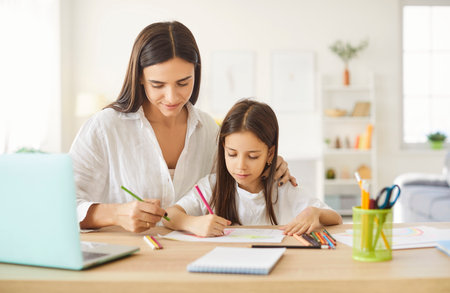 Mother and child doing school homework together. Little girl together with mom sitting at desk and drawing picture with colored pencils. Family, education conceptの写真素材