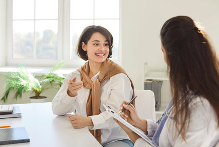 Woman during clinic visit, female doctor talking to patient, explaining prescription, medical screening, examination result, giving consultation, girl visiting practitioner, explain, making notesの写真素材