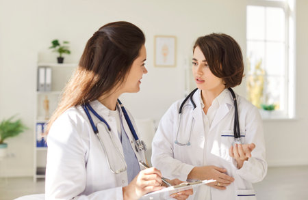 Consulting colleagues, young positive practitioner female doctor and nurse discussing patient, explaining checkup result, medical screening, giving consultation on appointment, professional guidanceの写真素材