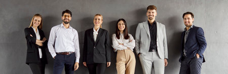 Six professionals, dressed in formal attire, stand confidently in a modern office against a gray wall. They share a moment of camaraderie and teamwork during working hours.の写真素材