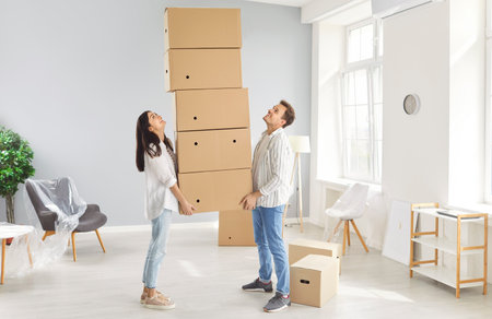 Young family, husband and wife holding cardboard boxes heap stack excited to move new modern flat, happy couple has fun, feels cool relocating together to first own house, apartment renters packingの写真素材