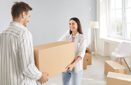 Young happy smiling couple carrying unpacking cardboard boxes in new apartment celebrating moving day. Cheerful family buy a property. Move, relocating, real estate, mortgage concept.の写真素材