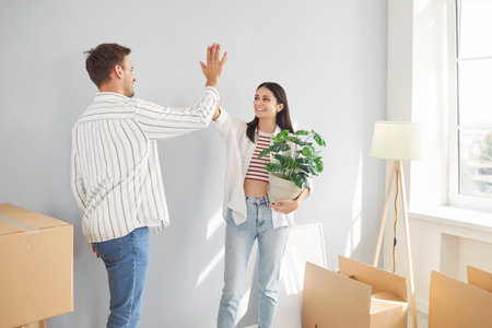 Young family, husband and wife surrounded by cardboard boxes excited to move new modern flat, happy couple have fun high five, feels cool relocating together to first own house, apartment rentersの写真素材